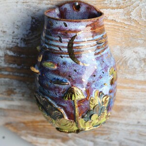 May include: A ceramic wall planter with a blue and purple glaze. The planter is decorated with gold accents and a mushroom design.
