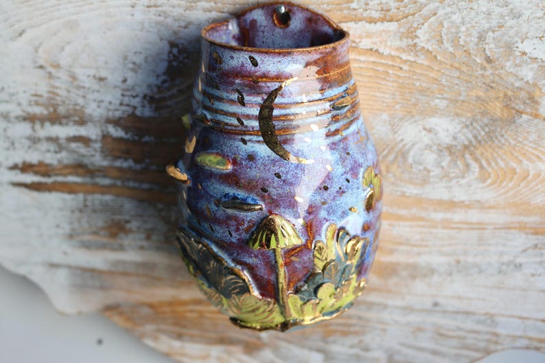 May include: A ceramic wall planter with a blue and purple glaze. The planter is decorated with gold accents and a mushroom design.