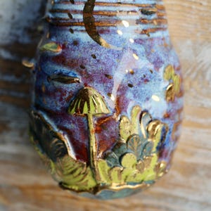 May include: A ceramic ornament with a blue, purple, and gold glaze. The ornament features a mushroom design with gold accents.