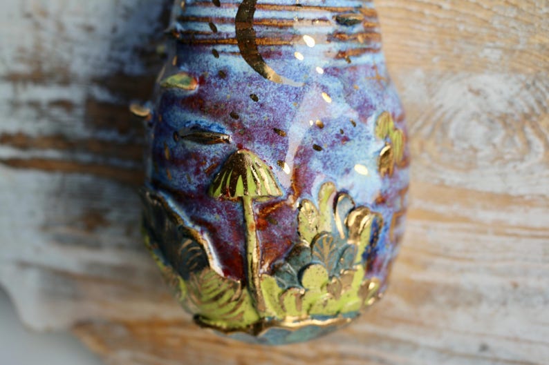 May include: A ceramic ornament with a blue, purple, and gold glaze. The ornament features a mushroom design with gold accents.
