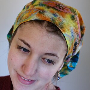 May include: A patterned head covering in shades of yellow, orange, blue, and green. The fabric looks soft, possibly cotton or a similar textile. The head covering is designed to fit snugly around the head, offering a comfortable fit.