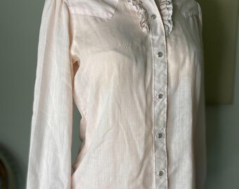 May include: A pale pink, long-sleeved button-up shirt with a ruffled collar and a striped pattern.
