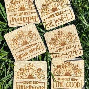 Puede incluir: Seis posavasos cuadrados de madera con diseños florales grabados con láser y citas inspiradoras: "Choose Happy", "Be Real, Not Perfect", "Remember Your Worth", "You Are Enough", "Enjoy the Little Things" y "Focus on the Good".