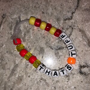 May include: A red, yellow, and orange beaded bracelet with the words "THAT'S CUTE" spelled out in white letters.