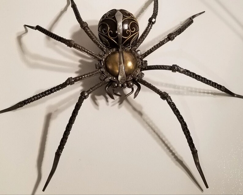 May include: A large metal spider sculpture with a black and gold body and eight long, thin legs. The spider is made of welded metal and has a detailed design.