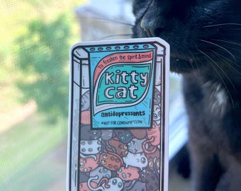May include: A rectangular sticker with the text "Kitty Cat antidepressants" and the phrase "To freshen the spirit & mind." The sticker features cartoon cat illustrations in various colors. A black cat is in the background.