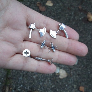 May include: A set of silver earrings featuring a screw, two ants, and two miniature axes.
