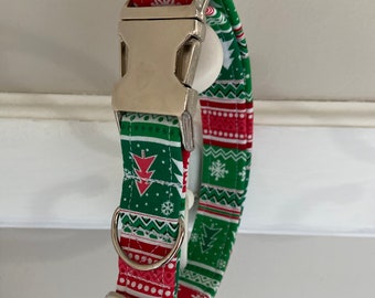 May include: A green and red dog collar with a white snowflake and Christmas tree pattern. The collar has a silver buckle and a silver D-ring.