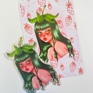 Peut inclure: Deux autocollants holographiques représentant une femme aux cheveux verts avec des détails de fraises. La femme porte une couronne de feuilles vertes et a un visage rose avec des yeux verts. Les autocollants sont sur un fond blanc avec un motif de fraises roses.