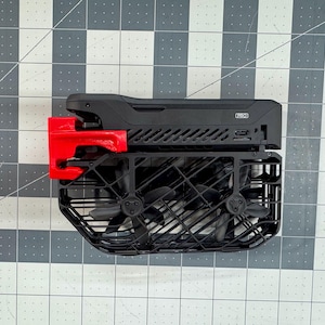 Peut inclure: Un drone noir avec une cage de sécurité rouge et quatre hélices. Le drone a un corps noir avec une garniture argentée et une cage noire et argentée. Les hélices sont noires et ont une garniture argentée.