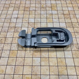 May include: A gray 3D printed plastic object with a complex design, featuring multiple openings and a circular hole. The object is lying on a beige tiled surface.