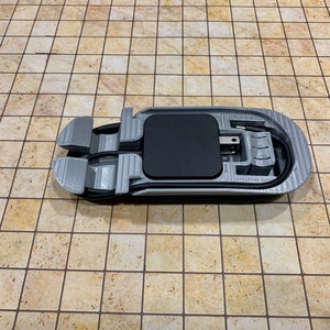 May include: A 3D printed gray plastic holder for a phone charger with a black charging pad and a black cord.