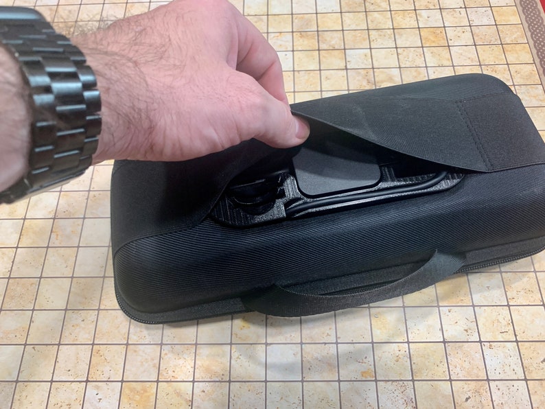 May include: A black zippered carrying case with a handle and a flap that opens to reveal a black interior with compartments.