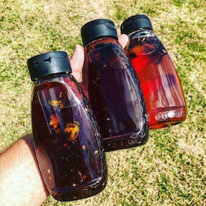 May include: Three glass bottles with black lids filled with dark liquid. The bottles have a honeycomb pattern on the bottom.