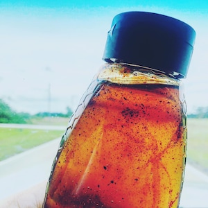 May include: A glass bottle with a black lid filled with a dark brown liquid. The liquid has a speckled appearance.