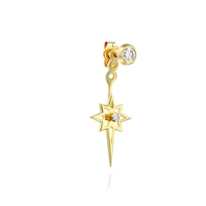 Könnte beinhalten: Goldener sternförmiger Ohrring mit einem kleinen Diamanten in der Mitte. Der Ohrring hat einen baumelnden Sternanhänger mit einem Diamanten in der Mitte.