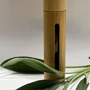 May include: A wooden roller bottle with a clear glass insert. The bottle is sitting on a white surface with a sprig of sage leaves.