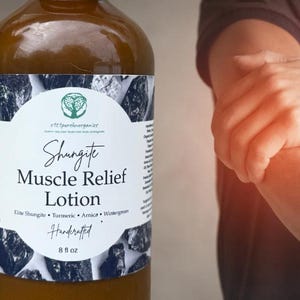 Peut inclure: Une bouteille en verre marron de lotion Shungite Muscle Relief, environ 237 ml, avec une &eacute;tiquette blanche orn&eacute;e de graphiques de pierres noires et grises. L'&eacute;tiquette indique "Elite Shungite, Turmeric, Arnica, Wintergreen" et "Handcrafted".
