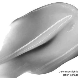 Peut inclure: Gros plan d'une tache de lotion lisse et de couleur claire sur fond blanc. La lotion a un &eacute;clat brillant et semble fra&icirc;chement appliqu&eacute;e. Le texte en bas indique : "La couleur peut l&eacute;g&egrave;rement varier, car chaque lotion est fabriqu&eacute;e &agrave; la main."