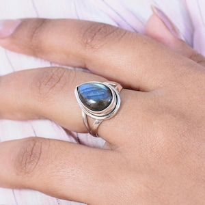 Peut inclure: Une bague en argent avec une pierre précieuse en labradorite bleue en forme de larme. La bague a un design simple avec une bande lisse.