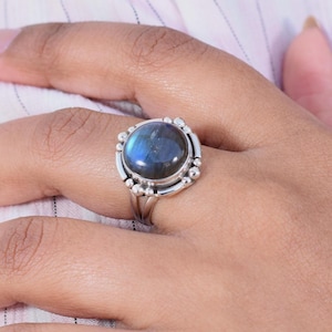 May include: A silver ring featuring a round, dark blue labradorite gemstone set in a beaded bezel.