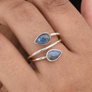 May include: A silver ring with two teardrop-shaped blue gemstones. The ring is designed to wrap around the finger.