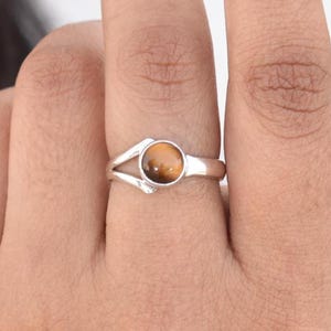 May include: A silver ring with a round, brown tiger's eye gemstone. The ring has a delicate, open design.