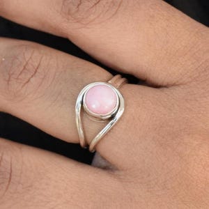 May include: A silver ring with a pink gemstone set in a curved band.