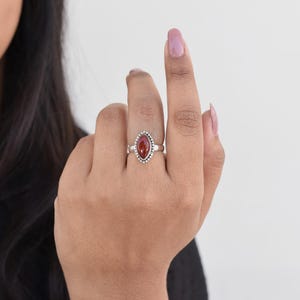 May include: A silver ring with a red gemstone set in a beaded oval setting.