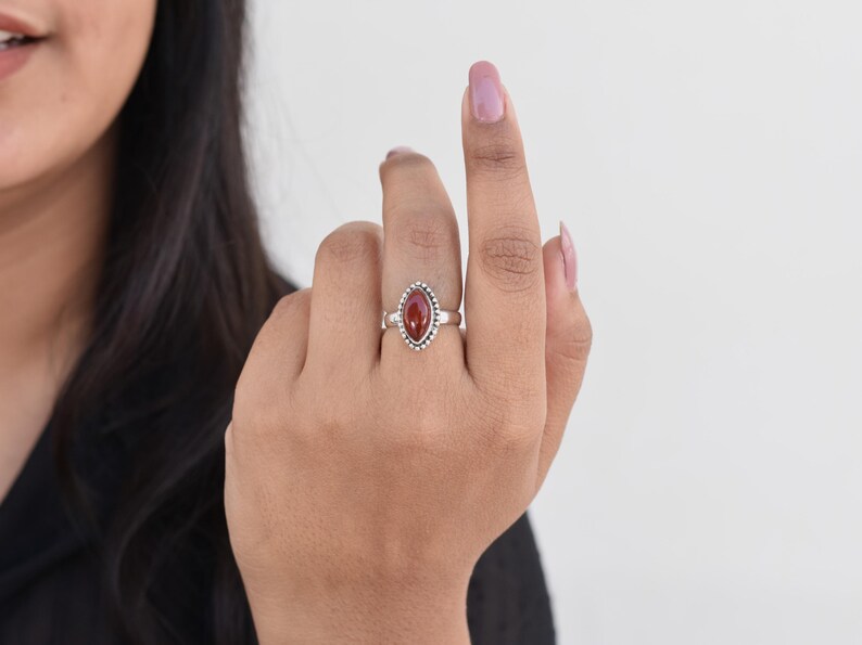 May include: A silver ring with a red gemstone set in a beaded oval setting.