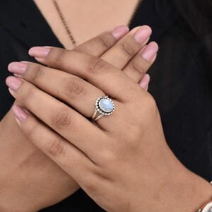 May include: A silver ring with a white oval moonstone set in a silver bezel. The ring is on a person's finger.