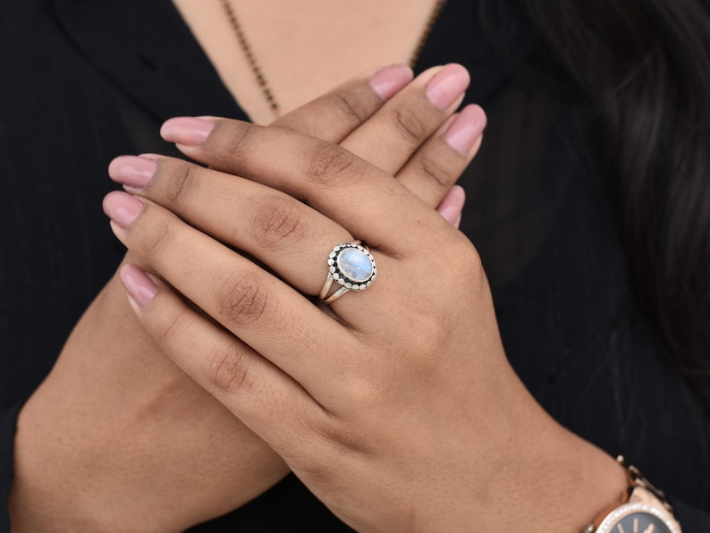 May include: A silver ring with a white oval moonstone set in a silver bezel. The ring is on a person's finger.