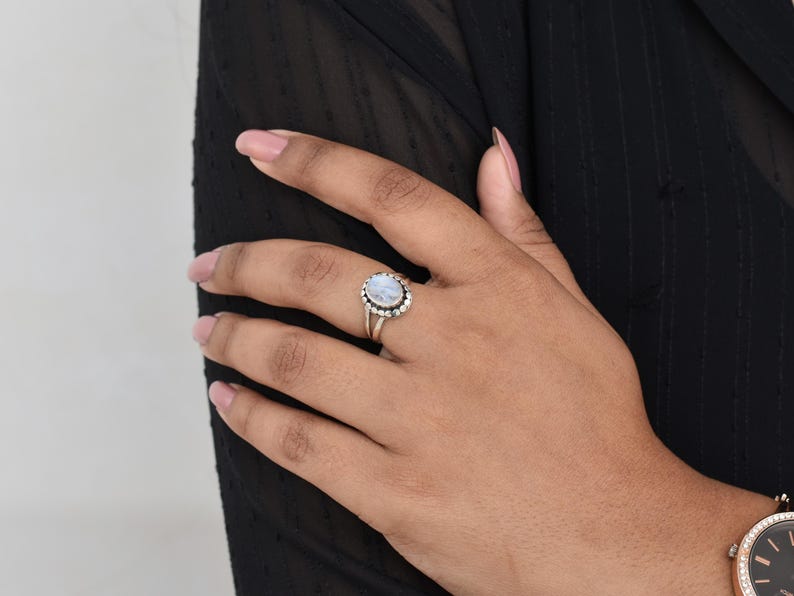 May include: A silver ring with a white oval moonstone set in a silver bezel. The ring is on a person's finger.
