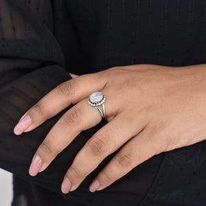 May include: A silver ring with a white oval moonstone set in a beaded halo.