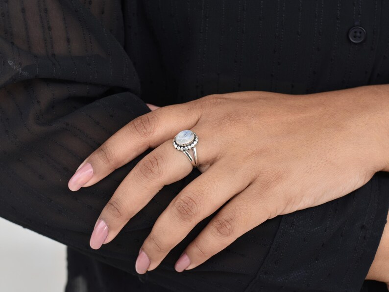 May include: A silver ring with a white oval moonstone set in a beaded halo.