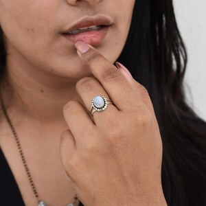 May include: A silver ring with a white oval moonstone set in a silver bezel. The ring is surrounded by a row of small silver beads.