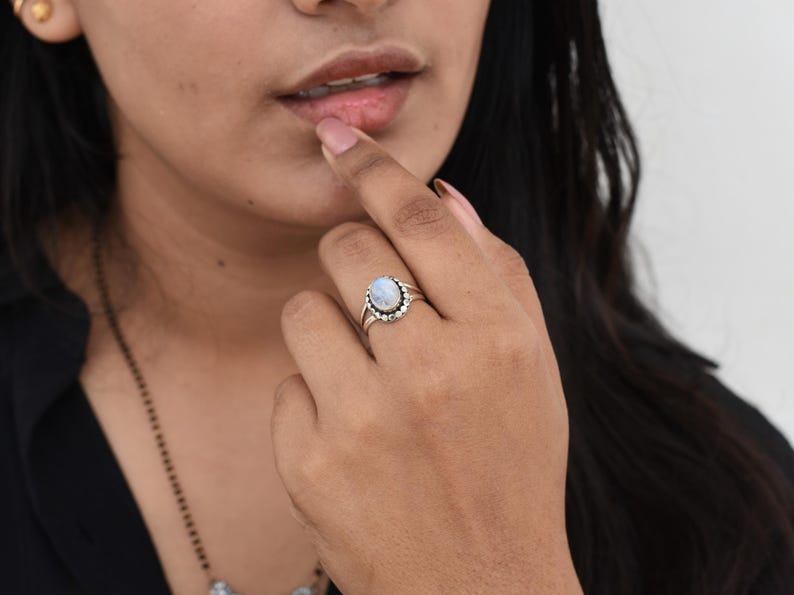 May include: A silver ring with a white oval moonstone set in a silver bezel. The ring is surrounded by a row of small silver beads.