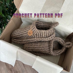 May include: A pair of brown crochet slippers with a tag, inside a cardboard box lined with white paper. The text "CROCHET PATTERN PDF" is displayed above the slippers.