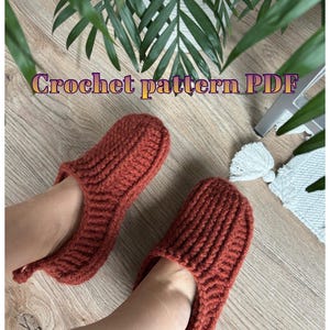 Op de afbeelding: Roodbruine gehaakte pantoffels met een geribbelde textuur. De afbeelding bevat de tekst "Crochet pattern PDF". De pantoffels worden getoond op een houten oppervlak, wat duidt op een handgemaakt item.