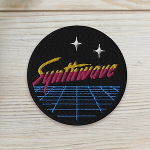 Può includere: Una toppa rotonda nera ricamata con la parola "Synthwave" in un font retrò con uno schema di colori blu e rosa. La toppa ha un motivo a griglia e due stelle gialle.