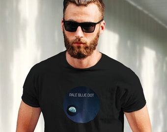 Puede incluir: Una camiseta negra con un gráfico de un planeta azul y blanco con el texto "Pale Blue Dot" encima.