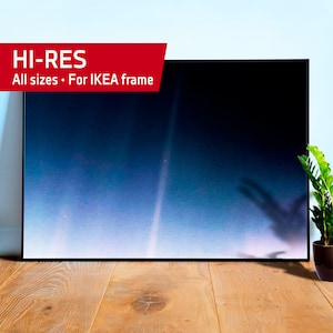 以下が含まれることがあります： 薄い青と白の画像が黒い額縁に入っています。画像の中央には細い白い線が走っています。画像は木製の床の上に置かれ、右側に茶色の鉢に入った緑の植物があります。