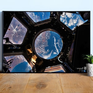 May include: A view of Earth from the International Space Station, seen through a circular window. The Earth is a blue and green sphere with white clouds, and the window is surrounded by the dark interior of the space station.