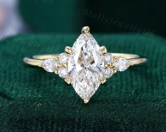 Könnte beinhalten: Ein goldener Verlobungsring mit einem großen, marquiseförmigen Diamanten als Mittelstein. Der Ring hat kleinere Akzentdiamanten, die um den Mittelstein und entlang des Bandes angeordnet sind. Auf dunklem, grünem Samthintergrund.