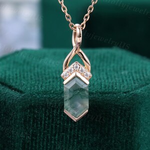 May include: Rose gold necklace with a geometric pendant featuring a green moss agate stone. The pendant is accented with small, clear gemstones. The necklace is displayed on a dark green velvet surface.