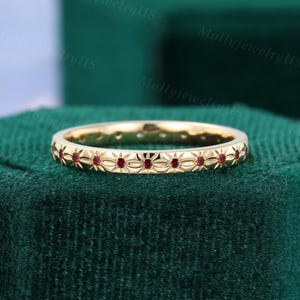 Può includere: Una sottile fascia d'oro con una fila di piccole pietre preziose rosse incastonate in un delicato motivo floreale.