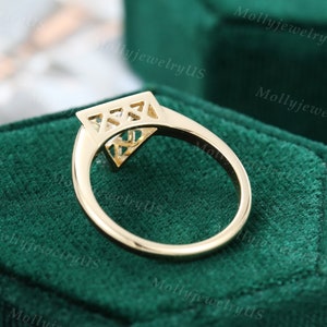 Pu&ograve; includere: Un anello di fidanzamento in oro con un diamante di forma quadrata incastonato in un design geometrico. L'anello &egrave; posto in una scatola per anelli in velluto verde.
