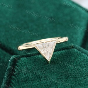 Pu&ograve; includere: Un anello d'oro con un diamante di forma triangolare. L'anello &egrave; su uno sfondo di velluto verde.