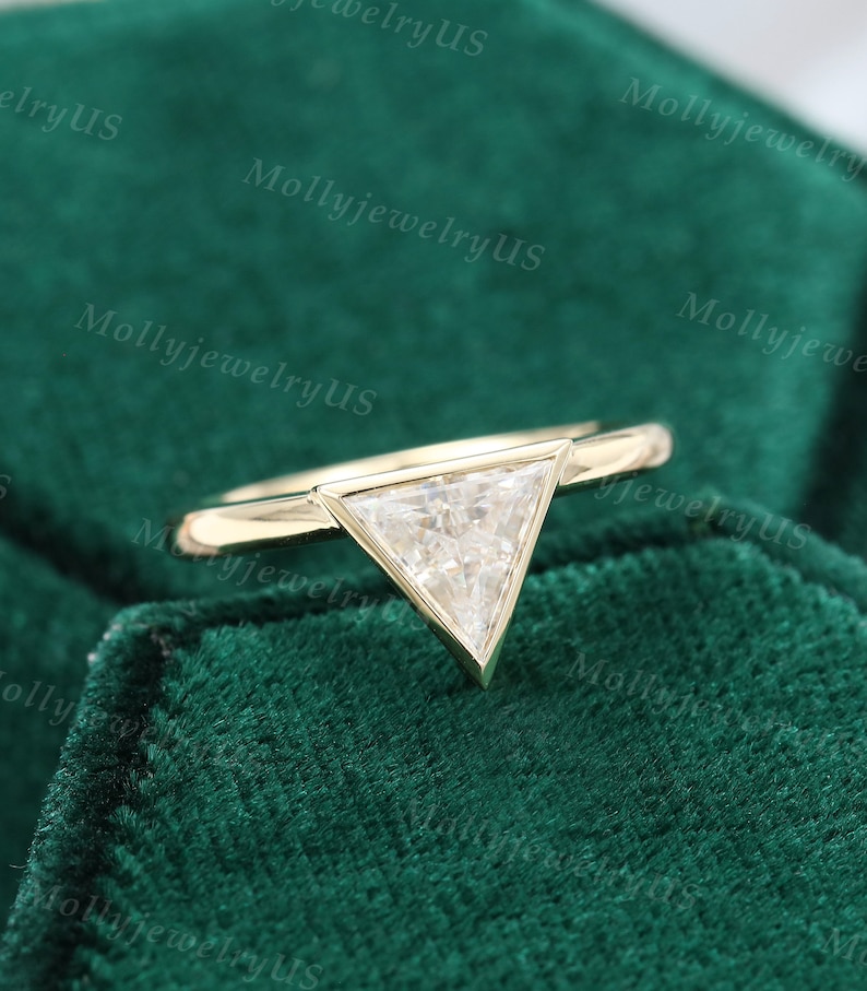 Pu&ograve; includere: Un anello d'oro con un diamante di forma triangolare. L'anello &egrave; su uno sfondo di velluto verde.
