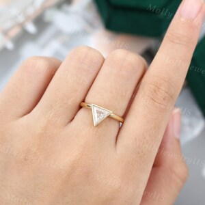 Pu&ograve; includere: Un anello d'oro con un diamante di forma triangolare incastonato in una montatura a bezel. L'anello &egrave; su un dito.